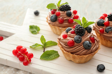 Tasty tartlets with chocolate cream and berries on white board