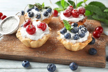 Tasty tartlets with berries on wooden board