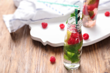 Glass bottle of fresh raspberry mojito on wooden table