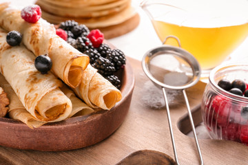 Plate with rolled thin pancakes and berries on table, closeup