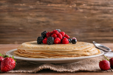 Plate with tasty thin pancakes and berries on wooden table