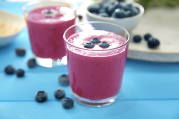 Glass with tasty blueberry smoothie on color wooden table