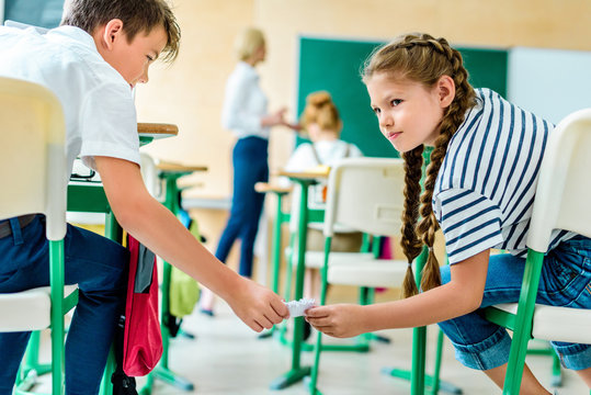 classmates passing message during lesson while teacher performing lecture