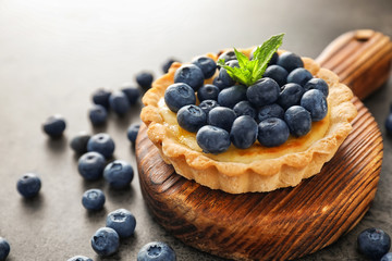 Wooden board with delicious blueberry tart on grey table