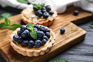 Wooden board with delicious blueberry tart on grey table