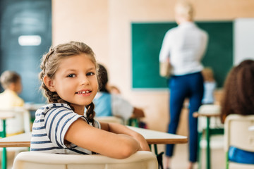 adorable little schoolgirl looking at camera during lesson