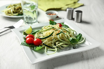 Plate of spaghetti with zucchini on white wooden table