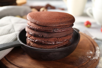 Frying pan with tasty chocolate pancakes on wooden board