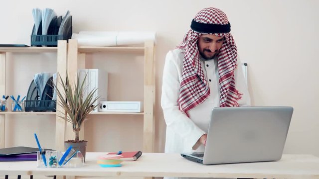 a modern Arabic office worker works on a laptop in the office. Muslim dressed in the national ghutra costume. khaliji style of appearance in the office
