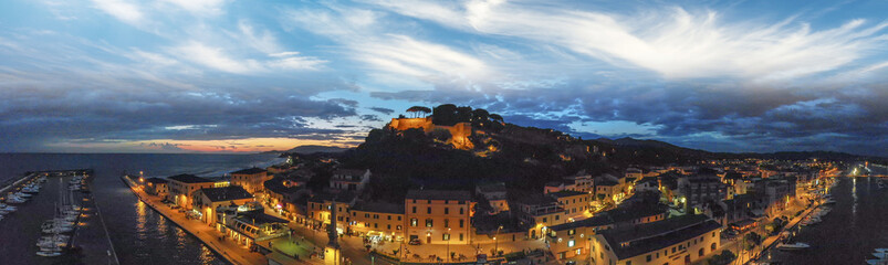 Panoramic aerial night view of Castiglione della Pescaia after sunset - obrazy, fototapety, plakaty