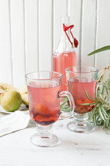 Two cups of summer plum lemonade. Decor of a green flower. Rustic. White wooden background.