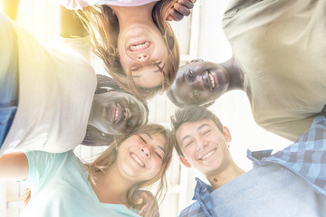 Upward view of five multi ethnic teenagers looking down, sun rays coming from behind