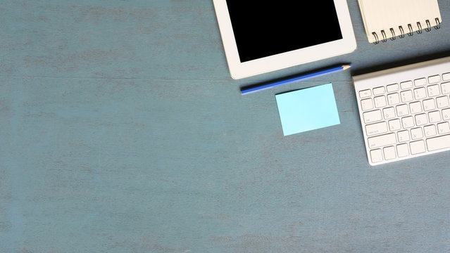 Office table Computer keyboard, tablet, pencil, sticky note and notebook paper on blue wooden table,Top view workspace.