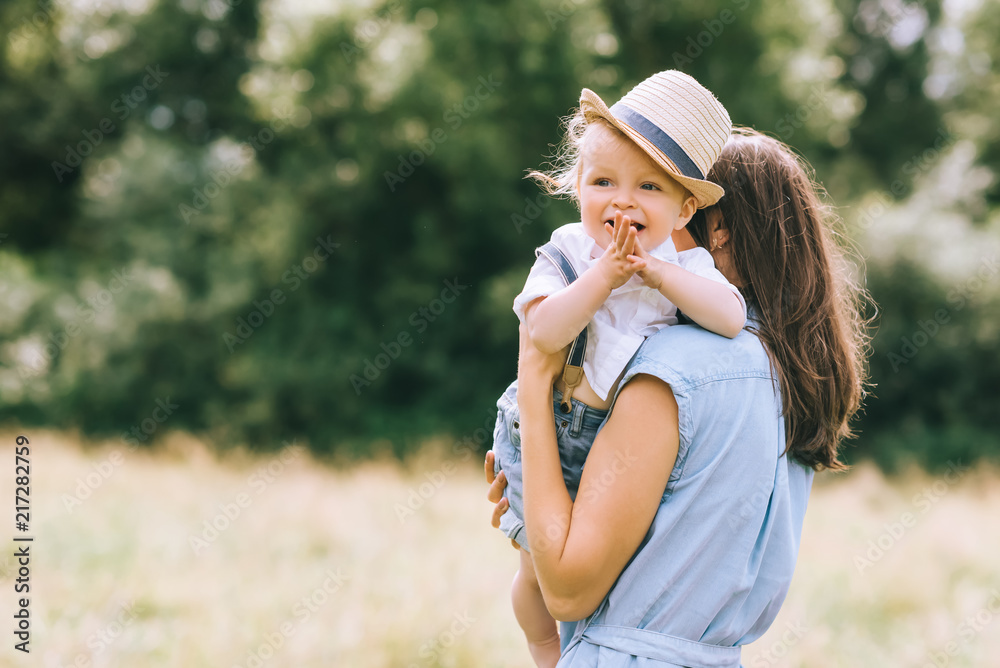 Wall mural mother holding son on hands and walking in field