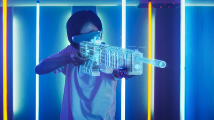 East Asian Pro Gamer Wearing Virtual Reality Headset and Holding Gun Hologram Plays Online Video...