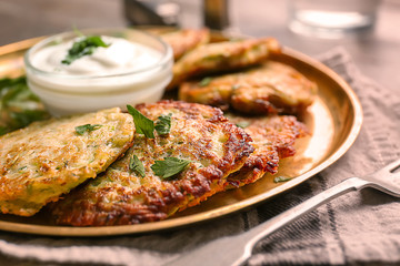 Metal tray with zucchini pancakes and sauce on table, closeup