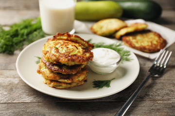 Plate with zucchini pancakes and sauce on wooden table