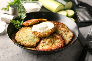 Plate with zucchini pancakes and sauce on table