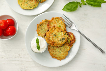 Plate with zucchini pancakes and sauce on wooden table