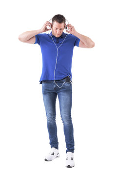 Relaxed young adult man putting on headphones attached to mobile phone in pocket looking down. Full body isolated on white background. 