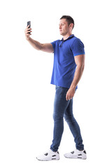 Confident young muscular casual man taking picture with mobile phone. Side view. Full body isolated on white background. 