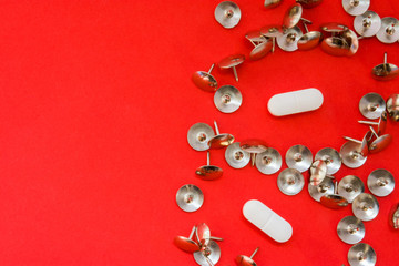 White pills surrounded by sharp thumbtacks at distance from them is on red background with empty area for headers top view. Concept images illustrating effect of painkillers and struggle with pain