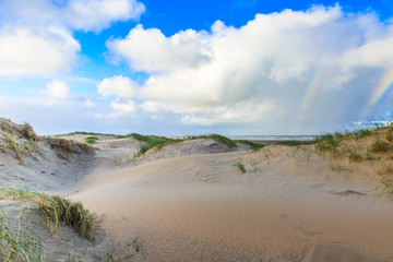 Newly formed Dunes on Dutch North Sea coast at IJmuiderslag with wind sweeping stripes in the sand  against the background of blue sky with scattered clouds and double rainbow