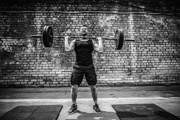Muscular fitness man doing deadlift a barbell over his head in outdoor, street gym. Functional...