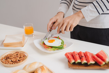 Hands of man cut the eggs on paper, served with bread, herbs, sausage and fresh juice.