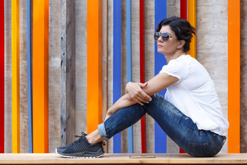 A brunette woman in jeans and sunglasses sits on a wooden stage