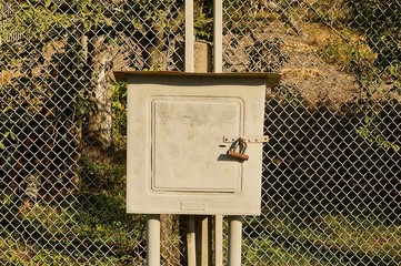 gray square iron box for electricity on a fence made of metal mesh