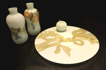 An apple on a plate and two white decanters decorated with Chinese art.