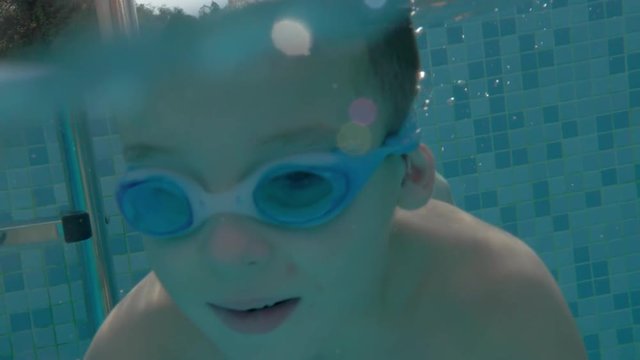 Slow motion shot of of the boy in goggles diving and swimming underwater. Bathing in pool on summer resort