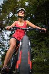 Naklejka premium Pretty, young woman riding her mountain bike on a forest path. Enjoying active leisure time outdoors.