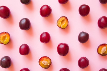 Fruit pattern of beautiful, fresh, whole and half of plums on pastel pink background. Healthy sweet...