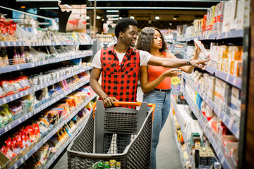 Family shopping for groceries in supermarket. Smiling african american couple with shopping trolley choosing food in supermarket