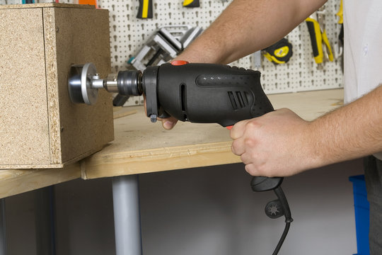 Worker with electric drill, drilling hole with hole saw, close up picture on hands and tool