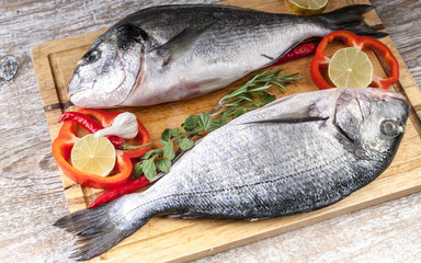 Dorado on a cutting board on a wooden table. Herbs, lime, cherry tomatoes, salt, paprika and spices. Close-Up