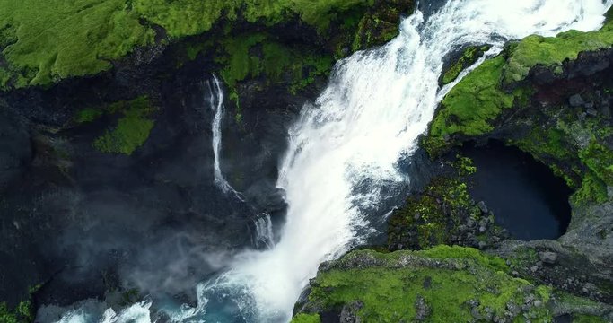 Top down aerial view of giant waterfall flowing in Iceland mountains filmed in slow motion