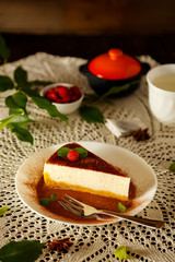 Slice of the classic cheesecake or New York cheesecake with a chocolate and cocoa powder on the top, fresh berries and mint, on a white plate, wooden table background