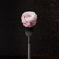 Homemade pink sweet marshmallow on fork on dark background with flying particles. Marshmallow, Meringue, Zephyr. Valentine's or Mothers Day. Wedding concept.