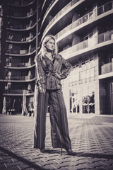Fototapeta na wymiar Beautiful girl in a stylish suit against a background of a blurry building. Stylish blonde. Fashionable girl. Everyday life of a beautiful girl. Lovely blonde in a stylish suit. Black and white.