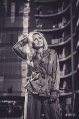 Beautiful girl in a stylish suit against a background of a blurry building. Stylish blonde. Fashionable girl. Everyday life of a beautiful girl. Lovely blonde in a stylish suit. Black and white.