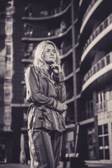 Fototapeta premium Beautiful girl in a stylish suit against a background of a blurry building. Stylish blonde. Fashionable girl. Everyday life of a beautiful girl. Lovely blonde in a stylish suit. Black and white.