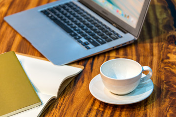 A cup of coffee with lab top and notebook on wooden table