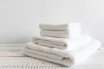 Folded white towels of different sizes on a white wooden table. Spa and wellness, cotton terry textile. Ecological theme