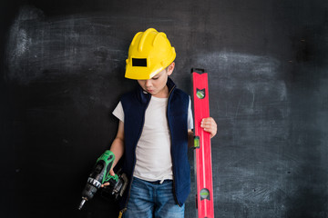 Young boy's standing with screwdriver in a helmet near blackboard. Young builder. Creative design concept of future profession