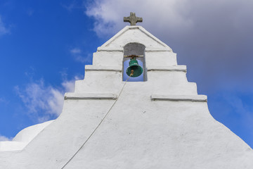 Bell tower at a Greek island against blue sky background.Green bell with Christian cross at a whitewashed bell tower of an Orthodox church at Mykonos island. © bestravelvideo