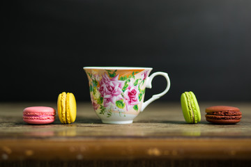 Cup of coffee and french macaron on old wooden table with black background, good morning