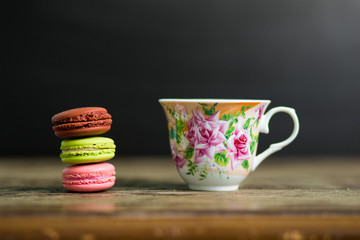 Cup of coffee and french macaron on old wooden table with black background, good morning